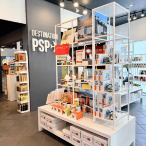 Retail display inside a modern store labeled "Destination PSP," showcasing architecture-themed books, souvenirs, and local products on white shelves.