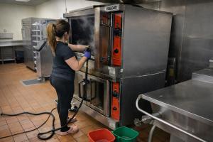 Technician performing deep cleaning of a commercial oven to remove grease buildup and ensure sanitary food preparation conditions