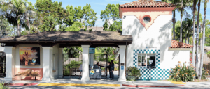 Entrance gate of a zoo or park with ticket booths, signage, and tropical landscaping on a sunny day.