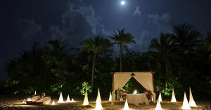 Private beach dining under a full moon at Grand Park Kodhipparu Maldives, with a candlelit cabana surrounded by glowing lanterns and palm trees