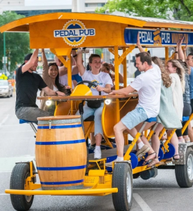 Group of guests pedaling and laughing aboard a Pedal Pub party bike during a guided city tour.