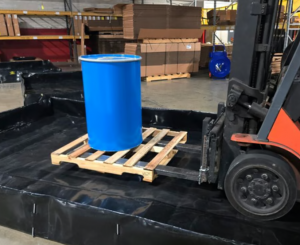 Mighty Berm in use protecting against a barrel spill while being moved by a forklift on a manufacturing floor.