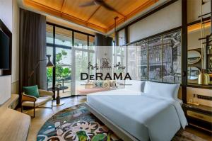 A luxurious guest room interior at DeRAMA Singapore featuring a king-sized bed, a balcony with lush greenery, and a decorative heritage wall mural showcasing traditional architecture.