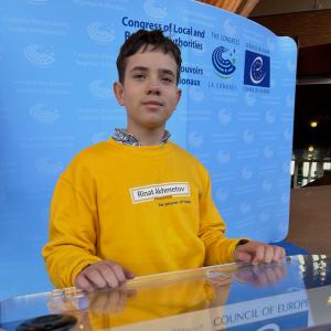 Illia Matviienko, the first Ukrainian child to be returned after being taken by russian forces, at the Council of Europe during the Mariupol Justice presentation. He is wearing a yellow sweatshirt with Rinat Akhmetov Foundation logo in the middle.