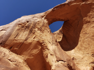 Close-up view of a curved sandstone arch with textured rock surface and deep shadows against a blue sky.
