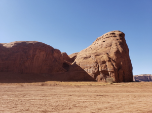 Large rounded red rock formations with smooth surfaces and small indentations set against a clear sky.