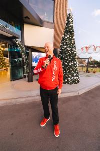 man holding microphone and speaking in front of a Christmas tree