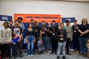 A group of high school students wearing name badges pose together indoors in front of a “Project MFG” banner, representing competitors at the 2026 Hawaii Maritime Welding competition.