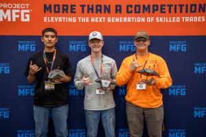 Three Maritime Welding Competition winners stand in front of a Project MFG backdrop holding welded metal projects. From left: Cyris Baltazar (third place) in a black shirt; Lucas Ziebold (Second Place) of Christian Liberty Academy in a gray shirt and cap;
