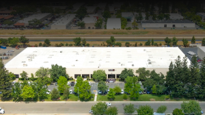 Aerial view of the Life-Assist headquarters building in Rancho Cordova, California, showing a large warehouse facility with surrounding parking, trees, and nearby canal.