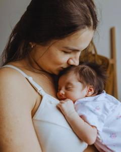 Mother holding her baby in a soft neutral nursery, representing the focus on protecting sensitive skin and preventing diaper rash.