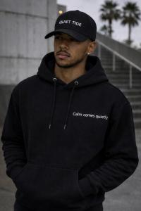 Black Quiet Tide hoodie with “Calm comes quietly” text in minimalist streetwear style