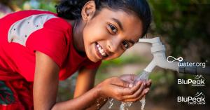 A little girl smiling, collecting water in the palm of her hands.