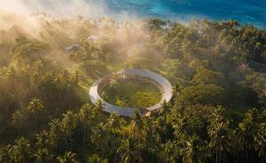 beams of sunlight illuminate a ring o-shape pavilion clad in solar photovoltaic modules. The setting is a Fijian coastal village.