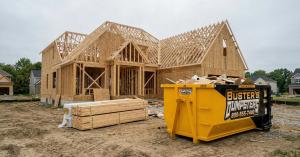 Buster's Dumpsters 20 yard roll-off dumpster next to a new home under construction with lumber stacks in Jackson County Michigan