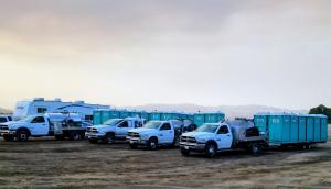 A line of Sierra Sanitation service trucks and portable restroom units parked in a flat, open field.