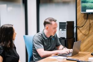 Robert Smith, a registered CMMC practitioner, is sitting at a computer with a local business owner, and helping walk through the CMMC 2.0 readiness proecess and documentation.