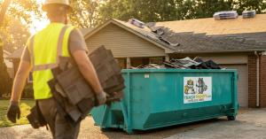 Roofer carrying shingles to Trash Pandy branded roll-off dumpster on residential driveway during roof replacement