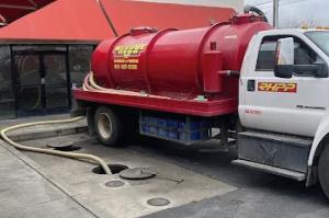 A red Rescue Hero pumping truck with hoses connected to underground septic access points.