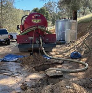 A red Rescue Hero septic pumping truck connected to a residential septic system with hoses and excavation tools nearby.
