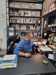Aldo Gutierrez working at his desk in the Porterville office, with a bookshelf featuring industry awards and a monitor showing a residential project.