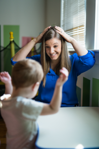 A woman is smiling while touching her head with both hands. There is the back of a child also touching his head with his hands.