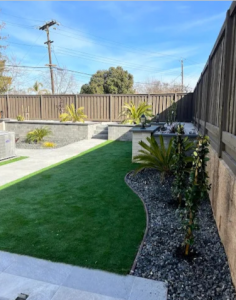 A high-end backyard transformation in California by Mike's Landscaping & Hardscape featuring a lush synthetic turf lawn bordered by a custom stone retaining wall and professional masonry.