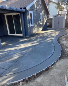 A newly installed dark grey concrete patio with a decorative curved edge alongside a residential home.