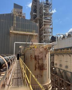 A wide shot of a large industrial plant featuring tall metal silos, structural towers, and overhead walkways under a blue sky. The image highlights the scale of facilities where Raw Welding provides expert crane and rigging support for turnaround and shut