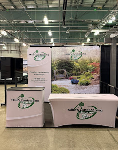 A professional trade show booth for Mike’s Landscaping & Hardscape featuring branded banners, a table cover with the company logo, and a large backdrop showing a landscaped garden with a wooden swing.