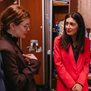 Two women in conversation inside the Empty Beds installation at the European Parliament. The installation's wardrobe, desk, and personal items are visible in the background.