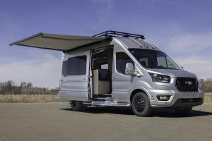 Ford Transit 350HD High Roof StarLux camper van by Waldoch Crafts parked on asphalt with its side door open and awning extended , featuring black wheels and a black metal roof rack.