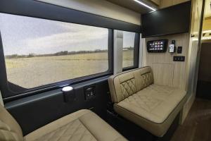 Interior view of the Waldoch StarLux camper van showing tan diamond-stitched leather seats, a wall-mounted Smart TV, and a digital touchscreen control panel next to large windows with privacy shades.
