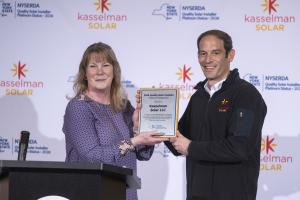 NYSERDA Associate Director of Quality and Market Standards Amy Kasson-Muzio presents the 2026 Platinum Quality Solar Installer plaque to Kasselman Solar President and CEO Steve Kasselman at the company's Menands, NY headquarters.
