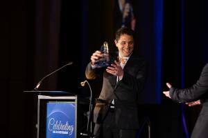 Max Lobovsky holds a glass award trophy while accepting his SME AM Industry Achievement Award.