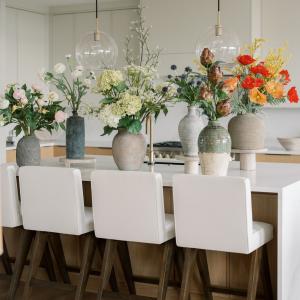 Kitchen island styled with faux floral arrangements in ceramic vases, featuring hydrangeas, poppies, and greenery in a modern luxury home.