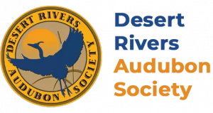 Logo for Desert Rivers Audubon Society. On the left is a circular gold seal containing a dark blue silhouette of a heron in flight over a sun and desert landscape. To the right, the text "Desert Rivers" appears in dark blue, and "Audubon Society" appears 