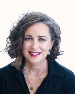 A smiling business woman wearing a black shirt and a necklace featuring a lion