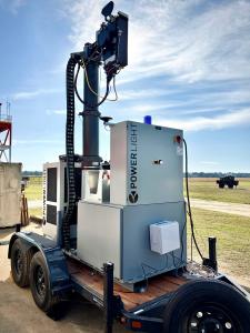 A laser transmitter stationed on the ground sending invisible laser light into the sky toward a receiver attached to a drone being used to power its battery