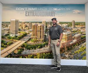 Chad Williams poses in front of a large wall graphic featuring the Richmond skyline and the phrase “Don’t wait until tomorrow be extraordinary today.”