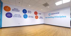 A branded interior wall for Indivior features the heading “Our Guiding Principles” alongside colorful icons and statements about teamwork, integrity, and decision-making.