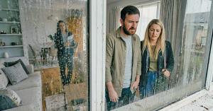 Photo of two prospective homebuyers standing outside a home and looking through visibly dirty windows while a real estate agent stands inside, illustrating how unclean glass can hurt buyer perception during a showing.