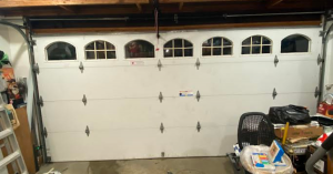 A skilled garage door technician carefully inspecting the hardware and hinges of a custom wooden carriage garage door on a historic Craftsman home.