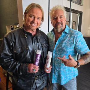 Just Jeff posing with television personality Guy Fieri while holding Formula 18 professional hair products inside a salon.