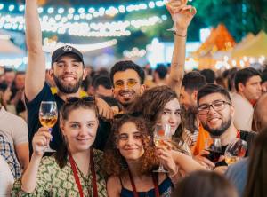 A group of happy friends smiling and toasting with their Yerevan Wine Days branded wine glasses in the crowded festival street area during the celebration in Armenia.