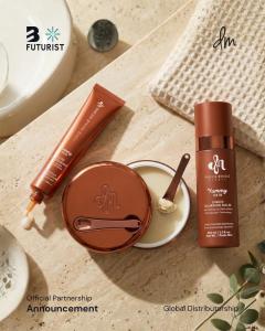 An overhead flat lay photograph of three Danessa Myricks Yummy Skin products arranged on a warm travertine surface: a serum tube, an open cream jar with a spatula, and a setting spray bottle. Products included: