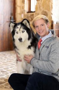 blonde man in a grey sweater sits with a malamute dog