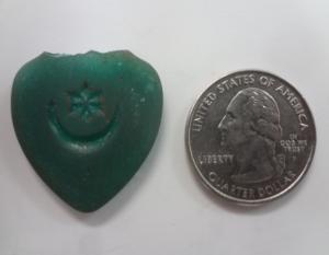 Green colored radioactive amulet pendulum next to quarter for size