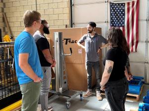 ENSER Business Development Engineer Domenic Arnone stands in ENSER’s warehouse speaking with Temple University engineering students beside a LiftTrac material handling system and LiftTrac equipment components.