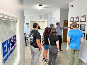 ENSER Project Manager Mike Wahner stands in a hallway at ENSER’s office, pointing to framed examples of past projects on the wall while a group of Temple University engineering students and faculty listen during a company tour.